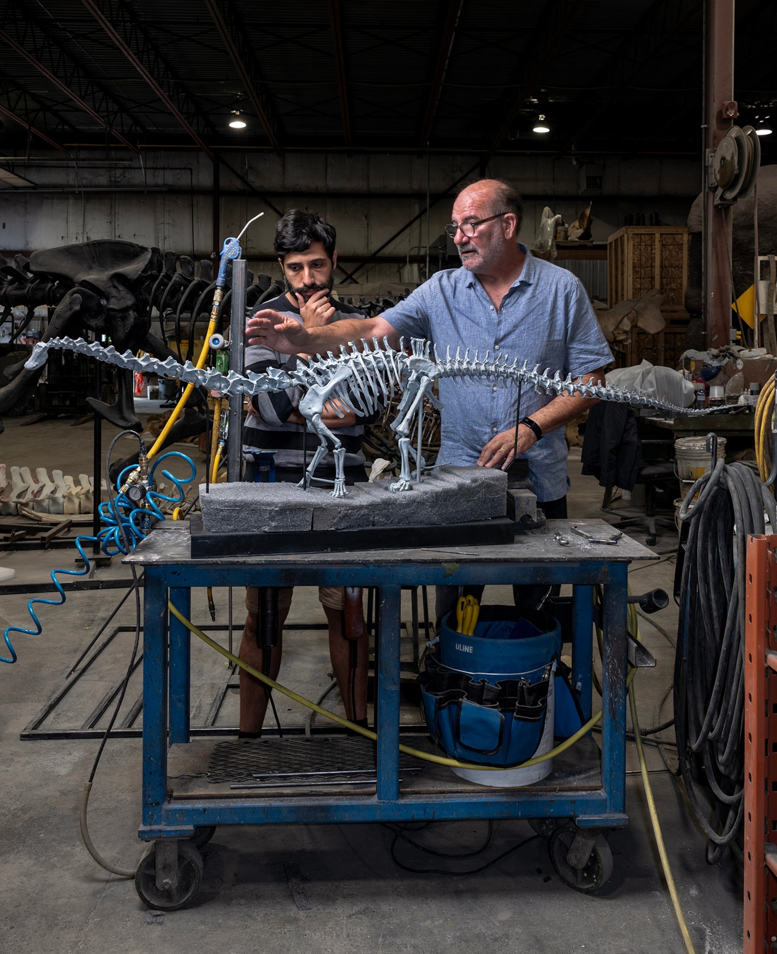 Two men study a medium-sized model of a dinosaur atop a table.