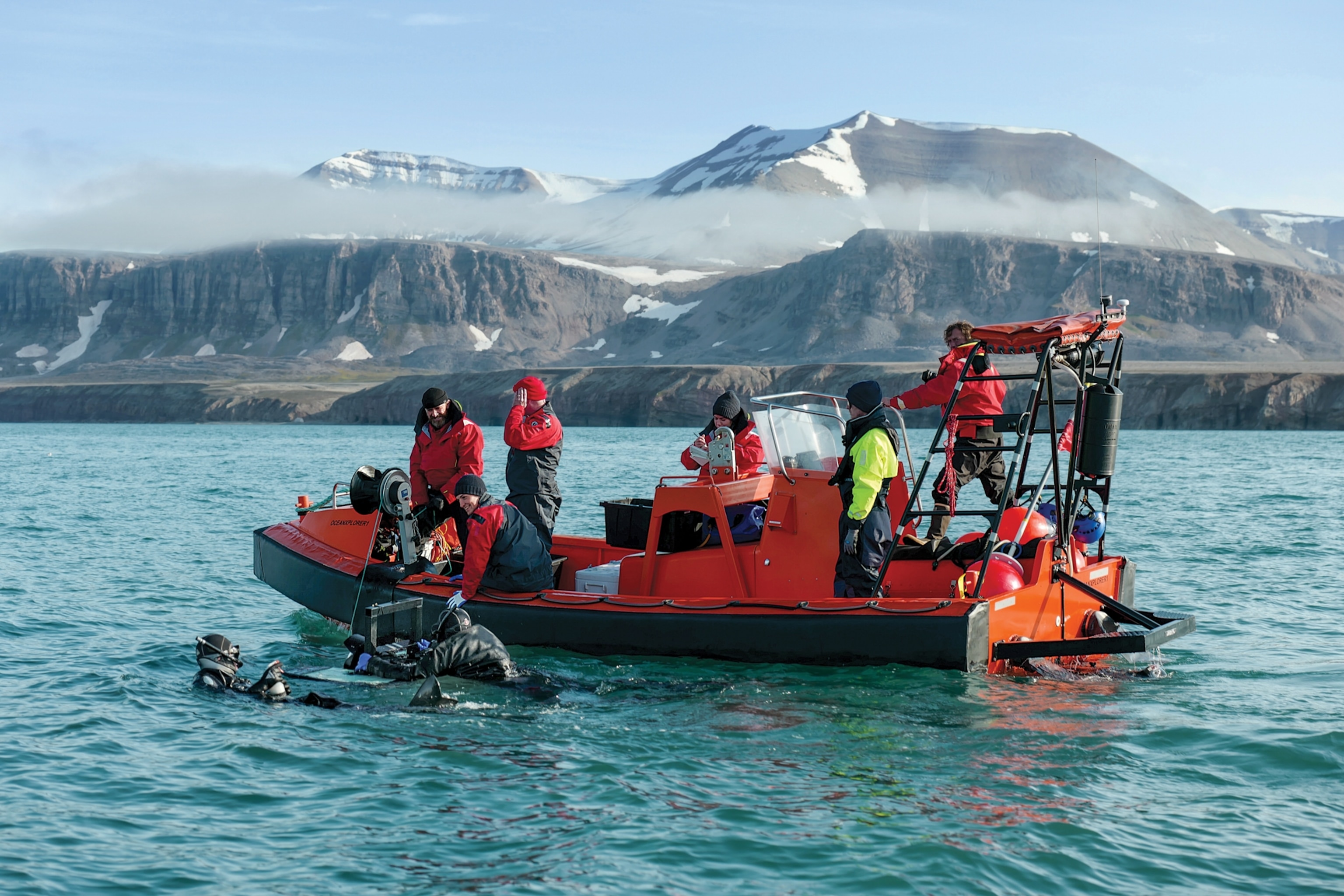 people in a small black boat and some people in the water as they put a tag on a shark this region is very cold